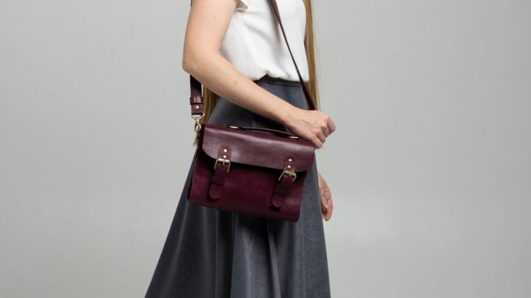 small red leather bag over a woman shoulder on a white background. shoulder handbag. woman in a white shirt and grey skirt and with a red handbag. style, retro, fashion, vintage and elegance.